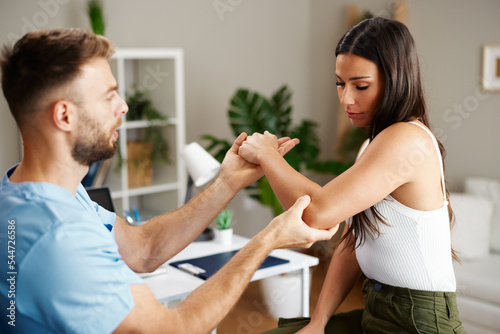 Tableau sur toile Young woman with elbow pain is being examined by a physiatrist