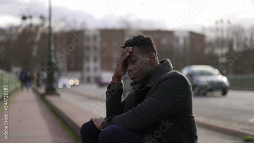 Anxious black man sitting on sidewalk feeling worried