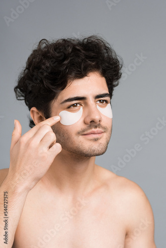 A young caucasian man with stubble beard placing patches under his eyes. Vertical view