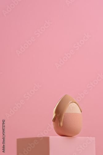 Slowly pouring liquid beige makeup foundation or bb cream on a sponge on light pink background. Texture of cosmetic bb or cc cream foundation liquid background 