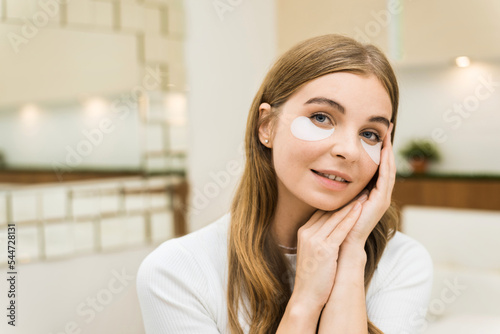 A young caucasian smiling woman with patches under her eyes looking into the camera. Skin care theme