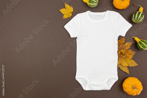 White baby girl or boy bodysuit flat lay mockup with pumpkins and fallen leaves on dark background. Design onesie template, print presentation mock up. Top view. 