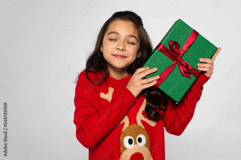 Pleased child in red sweater holding Christmas gift isolated on grey Pleased child in red sweater holding Christmas gift isolated on grey