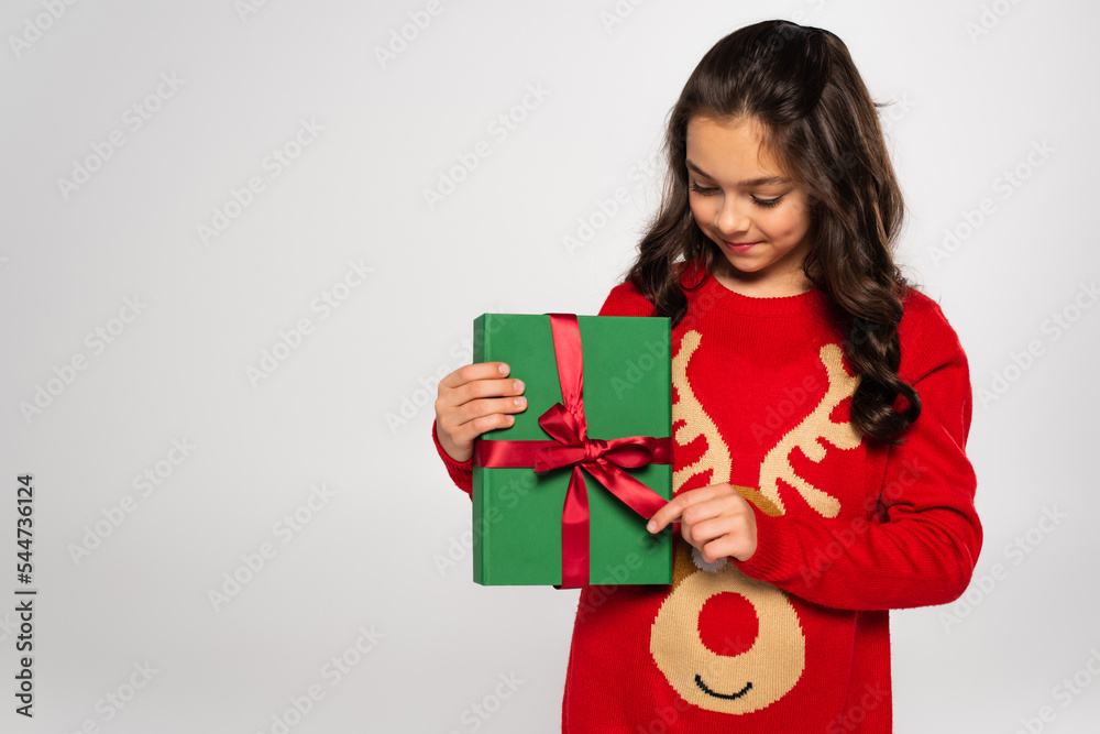 happy girl in red sweater looking at wrapped Christmas present isolated on grey happy girl in red sweater looking at wrapped Christmas present isolated on grey
