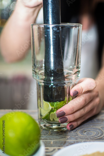 Bartender making refreshing coctail on a bar background. Dark moody style. Ice in tha glass