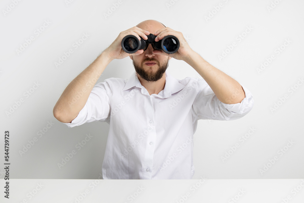 Young man looking through binoculars at table on white background Young man looking through binoculars at table on white background