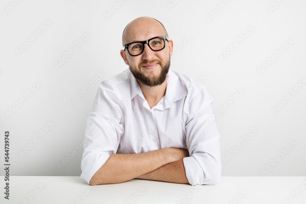 Smiling young man in glasses sitting at the table on a white background Smiling young man in glasses sitting at the table on a white background
