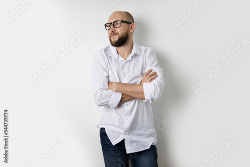Young bald man in a white shirt stands with his arms crossed on a white background