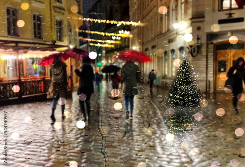 Rainy Christmas evening city street light people with umbrellas walk medieval Tallinn old town rain drops on shop windows glass Autumn season weather forecast
