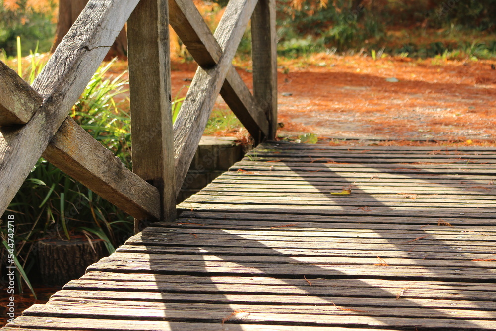 Wooden bridge in autumn park with shadows cast upon the planks. Low level view