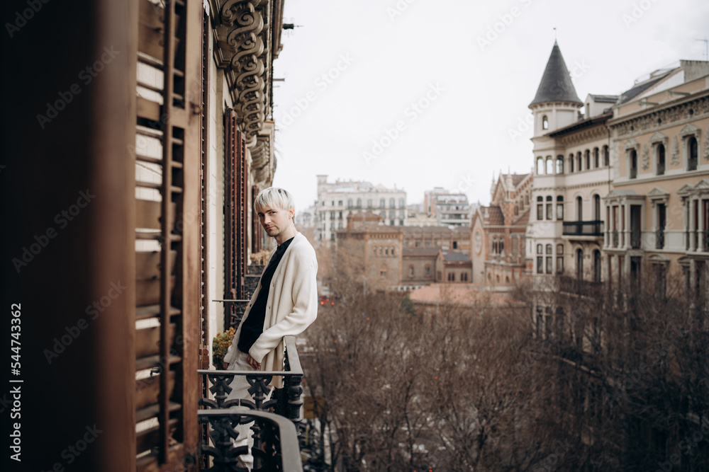 Blonde male standing on balcony, looking at camera.