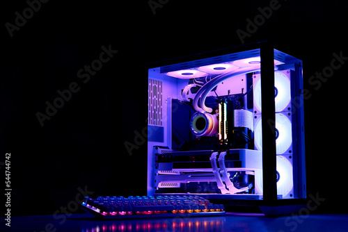 Gaming PC with RGB rainbow LED light. Liquid cooled computer. Powerful PC in a glass case with keyboard. Gamer\'s workplace in a dark room, neon light.