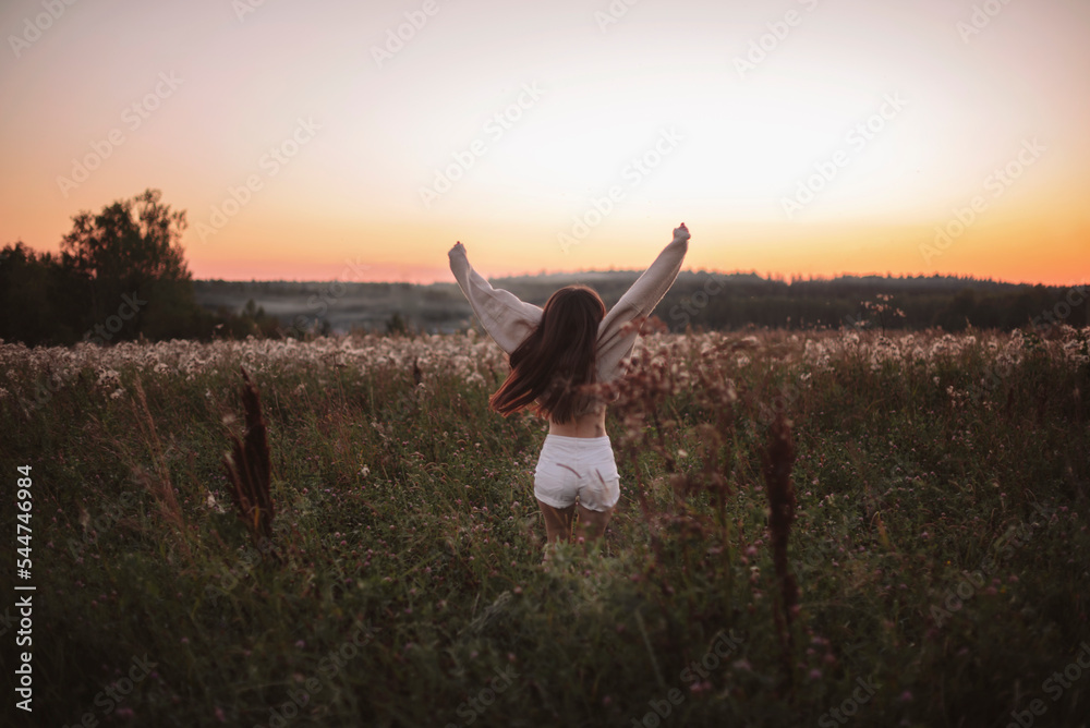 Girl with long brown hair enjoying nature on the Autumn field. Beauty Girl Outdoors raising hands in sunlight rays, Woman dressed in beige sweater Girl with long brown hair enjoying nature on the Autumn field. Beauty Girl Outdoors raising hands in sunlight rays, Woman dressed in beige sweater