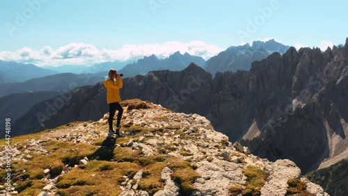 Woman stands on panoramic observation point shooting Three Peaks of Lavaredo and canyon with camera. Female tourist looks at mountain scenery aerial view photo