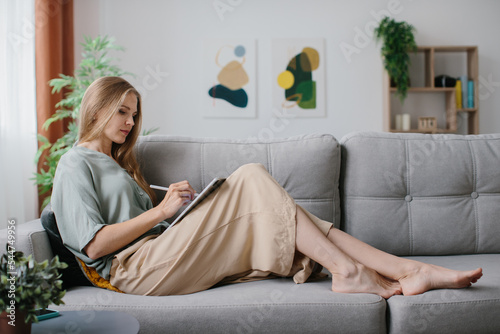 A girl sitting with a tablet and a stylus on the couch