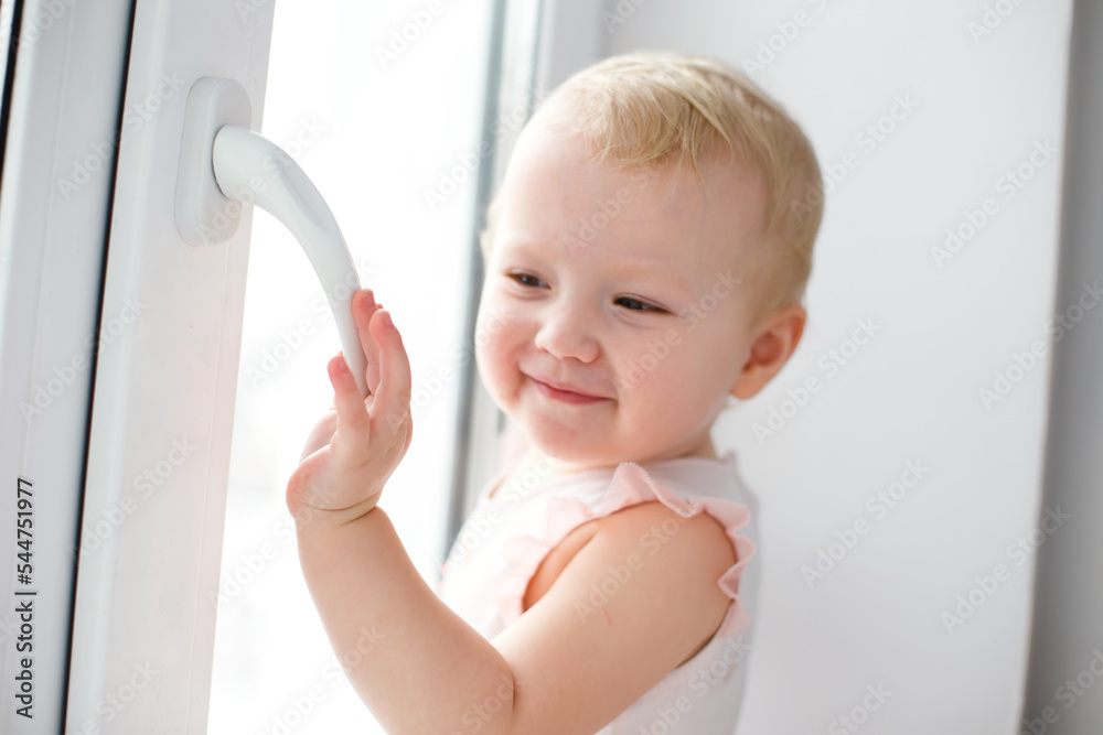 A little girl stands holding on to the handle of a broomtopplastic window. The danger of falling out of the window. The child stands on the windowsill on the high floor of the house A little girl stands holding on to the handle of a broomtopplastic window. The danger of falling out of the window. The child stands on the windowsill on the high floor of the house
