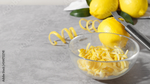 Bowl with peel pieces, fresh lemons and zester on grey table, space for text photo