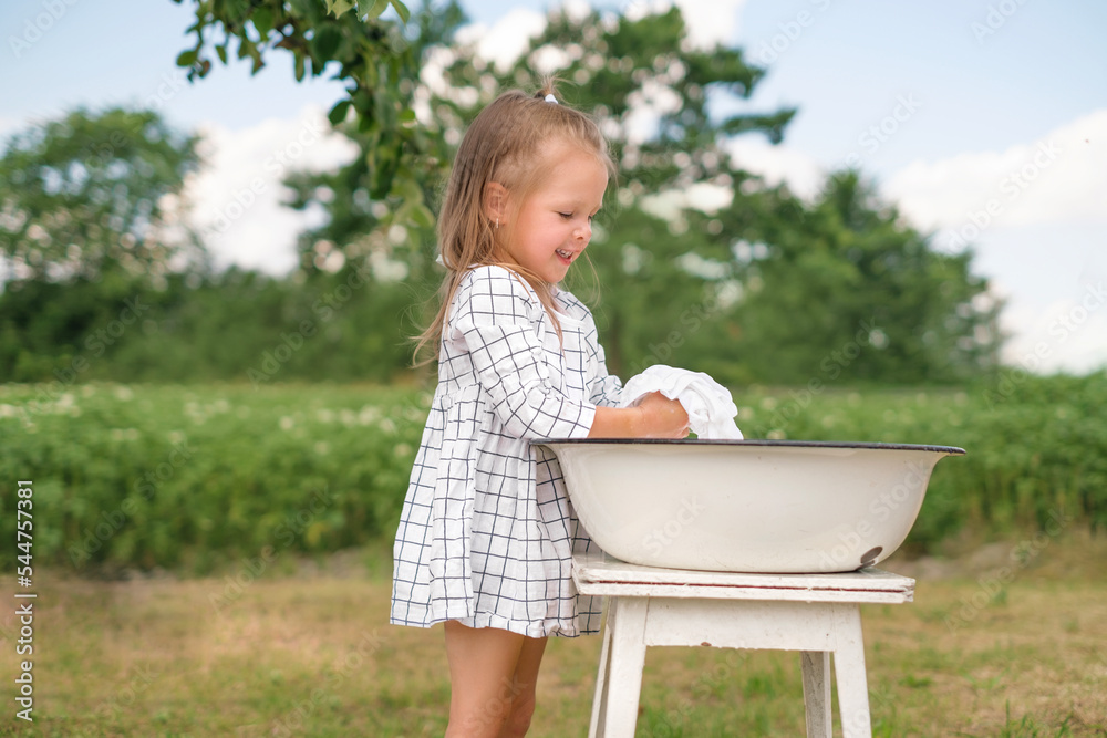 Funny laughing girl carefully washes clothes by hand in a basin outdoors in the fresh air on a hot summer day Funny laughing girl carefully washes clothes by hand in a basin outdoors in the fresh air on a hot summer day