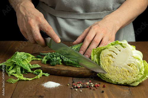 Female hands cutting Savoy cabbage on wooden table. Preparation of product for cooking.