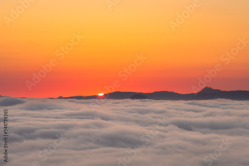 雲の彼方の山並みから昇る太陽