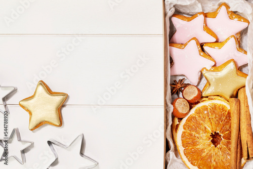 Hande made gift with home made cookies, dry fruits, nuts and cinnamon stiks on white wooden background with cookie cutters with copy space. Winter holiday pastries. Christmas cookies. Hand made gifts photo