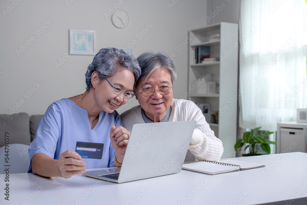 Happy Asian Senior couple at home. Handsome old man and attractive old woman are spending time together. Elderly couple with laptop and credit card in hands. Online shopping