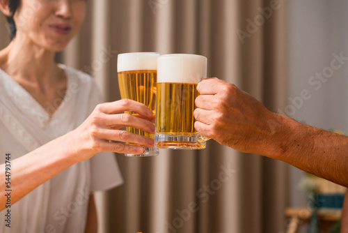ビールで晩酌をするミドル女性とミドル男性　夫婦の食事イメージ