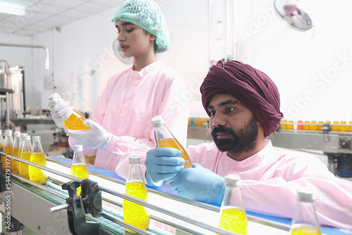 Asian man factory worker and woman expert quality staff is checking bottles line for beverage