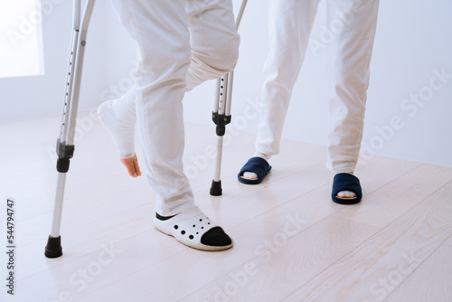 医者に介助されながら松葉杖をついて歩くミドル男性　リハビリイメージ
