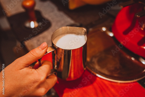 Metal Pitcher with white whipped milk in a woman's hand in a coffee shop