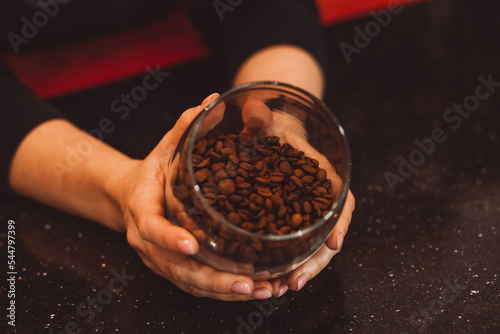 Glass jar with coffee beans in hands on dark background