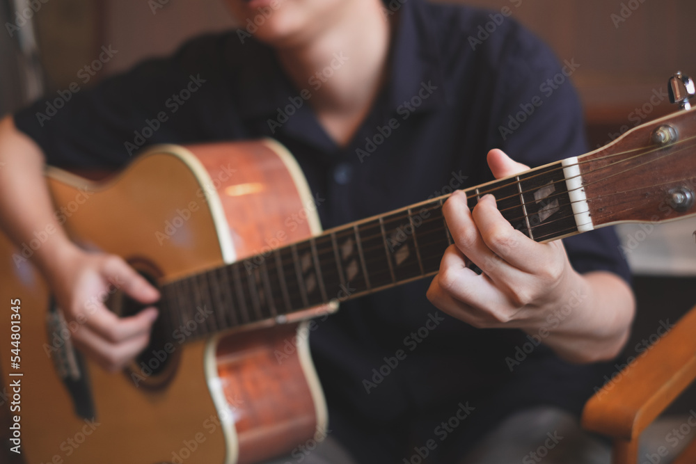 Fototapeta premium A close up of musician playing an acoustic guitar for entertainment or practicing for perfomance. Concept of indoor activity, lifestyle and leisure. A guitarist is focusing and enjoy playing guitar.