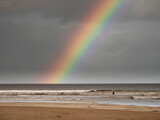 Colorful rainbow in the sky over dark ocean water. Surfers in the waves.