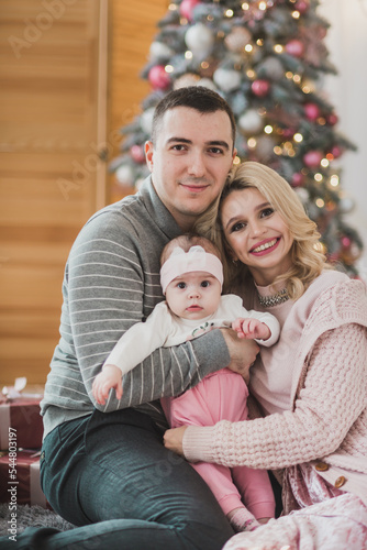 Family mom dad and little baby daughter near a beautiful Christmas tree. Stylish Christmas decorations in pink