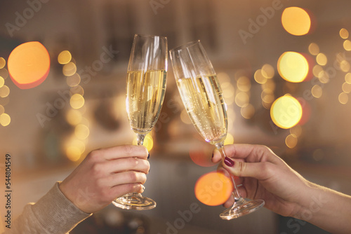 Fototapeta Two women clink glasses with champagne closeup  hands against the backdrop of a Christmas tree and lights