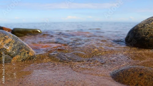 Close-up video. The wave rolls out onto the sandy shore with stones. High-quality shooting in Full HD.