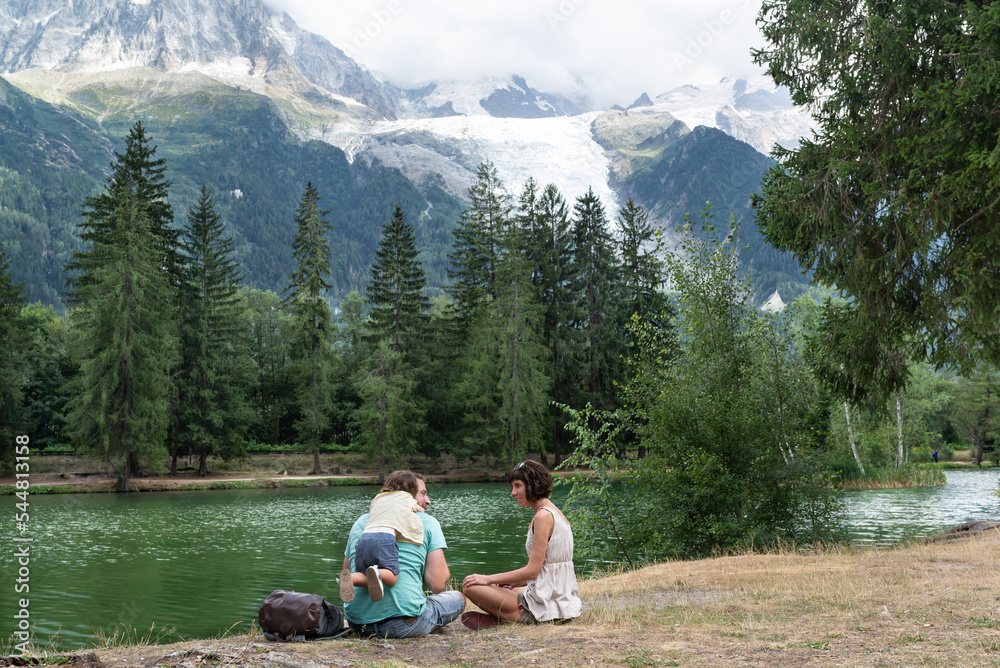 Father, mother and their little daughter playing close to a lake surrounded of mountains in french Alps. Lac des Gaillands, Chamonix.