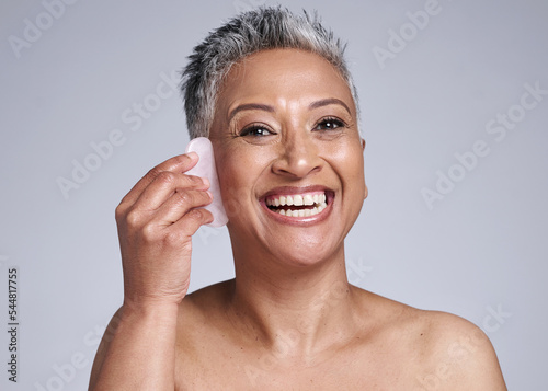 Beauty, gua sha and skincare of a senior woman in studio for dermatology, cosmetics and facial massage on a grey background. Face portrait of a mature model happy about skin results with rose quartz