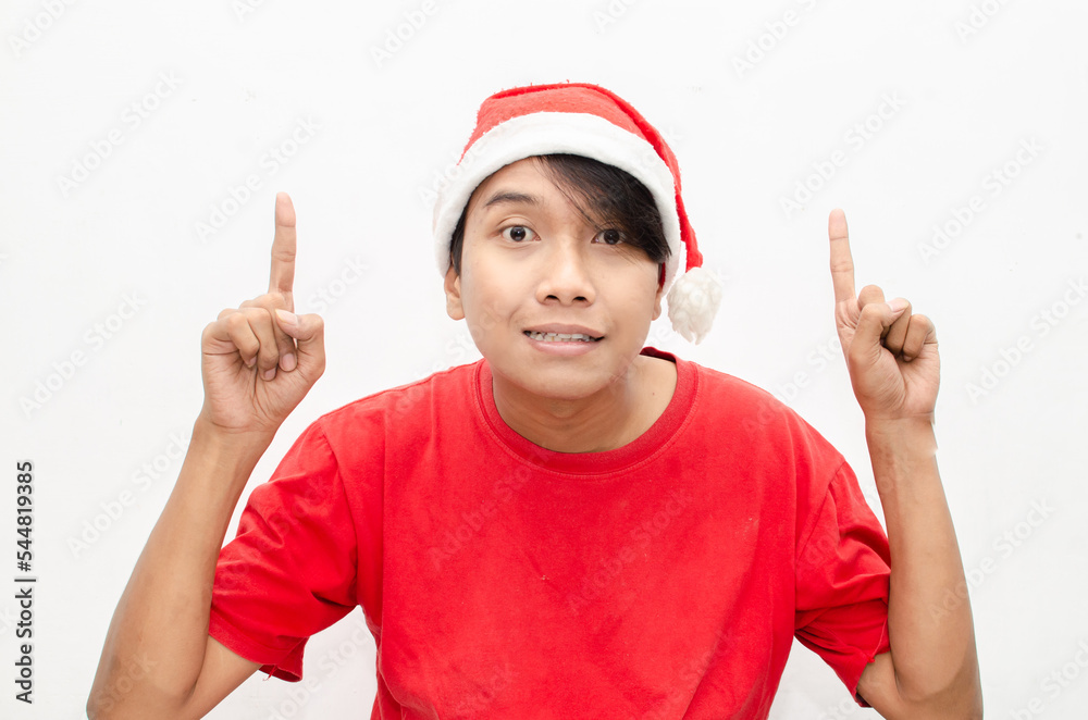 expressive happy young asian man in christmas santa theme clothes wit shocked, surprised and amazed face expression. wow expression man in red santa hat. christmas model concept for sale and discount. expressive happy young asian man in christmas santa theme clothes wit shocked, surprised and amazed face expression. wow expression man in red santa hat. christmas model concept for sale and discount.