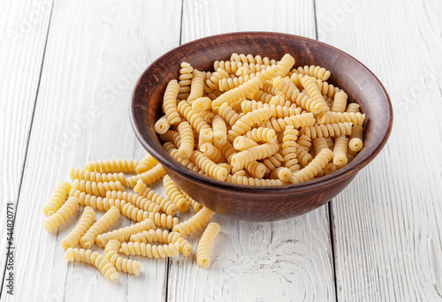 Uncooked fusilli pasta in ceramic bowl on white wooden background