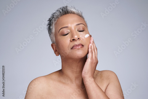 Senior woman, cream and skincare for health, wellness and hand touching smooth face against grey studio background. Elderly model, beauty and cosmetic lotion, advertisement and sunscreen with mockup