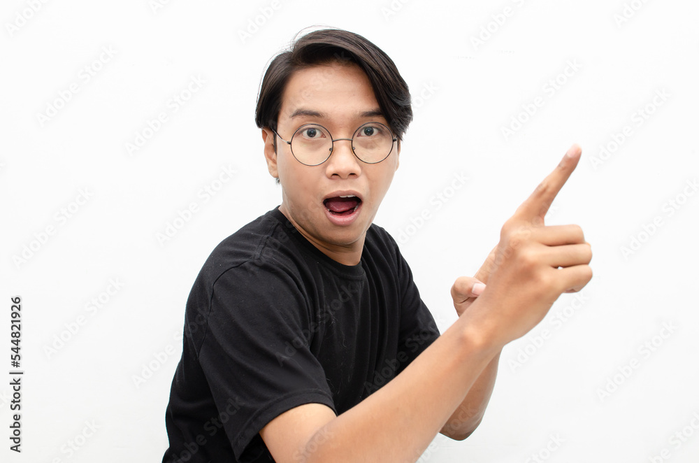 happy expressive asian young man with glasses shocked happily pointing finger to copy space offering something goods isolated over white background. billboard advertisment model concept. happy expressive asian young man with glasses shocked happily pointing finger to copy space offering something goods isolated over white background. billboard advertisment model concept.