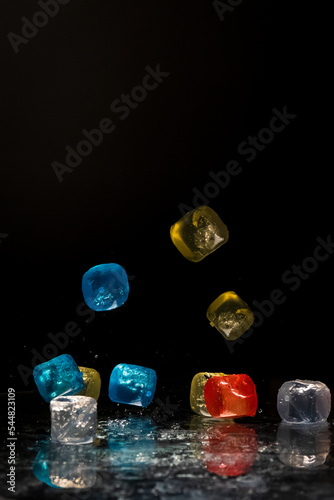 Falling colored cubes splashed with water on a black background. Red, yellow, blue and transparent. Conceptual, celebrated, commercial design