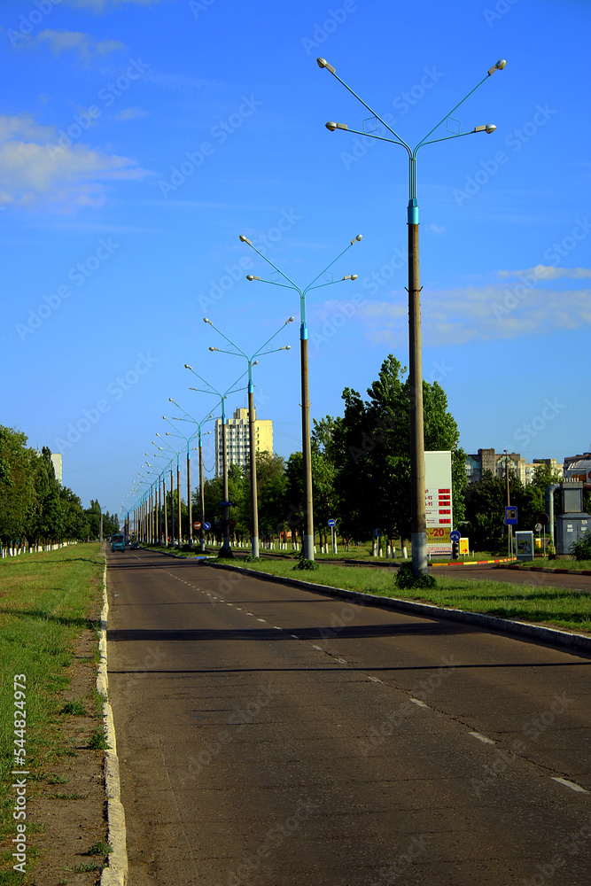 Road with lanterns and green spaces under blue sky	
