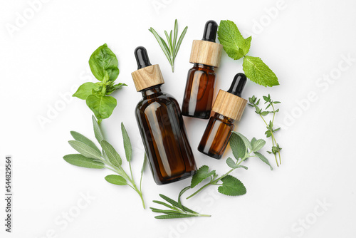 Bottles of essential oil and fresh herbs on white background, flat lay