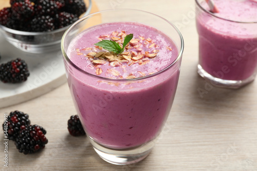 Delicious blackberry smoothie with oatmeal in glass on white wooden table, closeup
