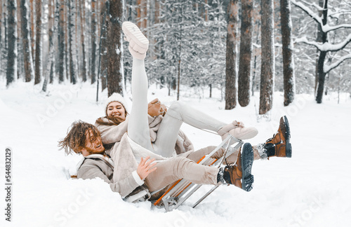 Love romantic young couple girl,guy in snowy winter forest with christmas tree, sled.Walking with sleigh in stylish clothes, fur coat,jacket, woolen shawl, bonnet.Snow lovestory.Romantic date,weekend