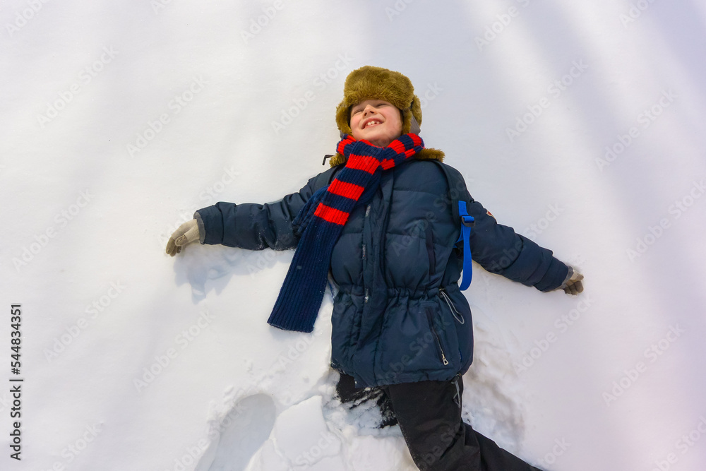 A boy lies in the snow and smiles. A child plays outside in winter A boy lies in the snow and smiles. A child plays outside in winter