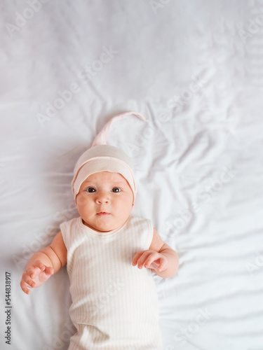 cute baby lies on the bed and pulls his hands, top view,pink hat and suit 