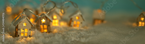 Fotografiet Abstract Christmas Winter Panorama with Wooden Houses Christmas String Lights in Cold Snow Landscape and Glowing Golden Lights in Background